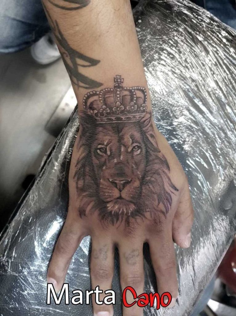 Tatuaje de un león con una corona estilo realismo en la mano