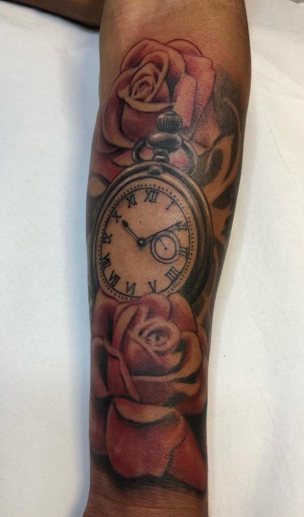 Tatuaje de un reloj rodeado de rosas estilo realismo a color en el antebrazo
