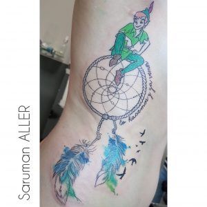 tatuaje watercolor o acuarela y a color de peter pan sentado sobre un amuleto