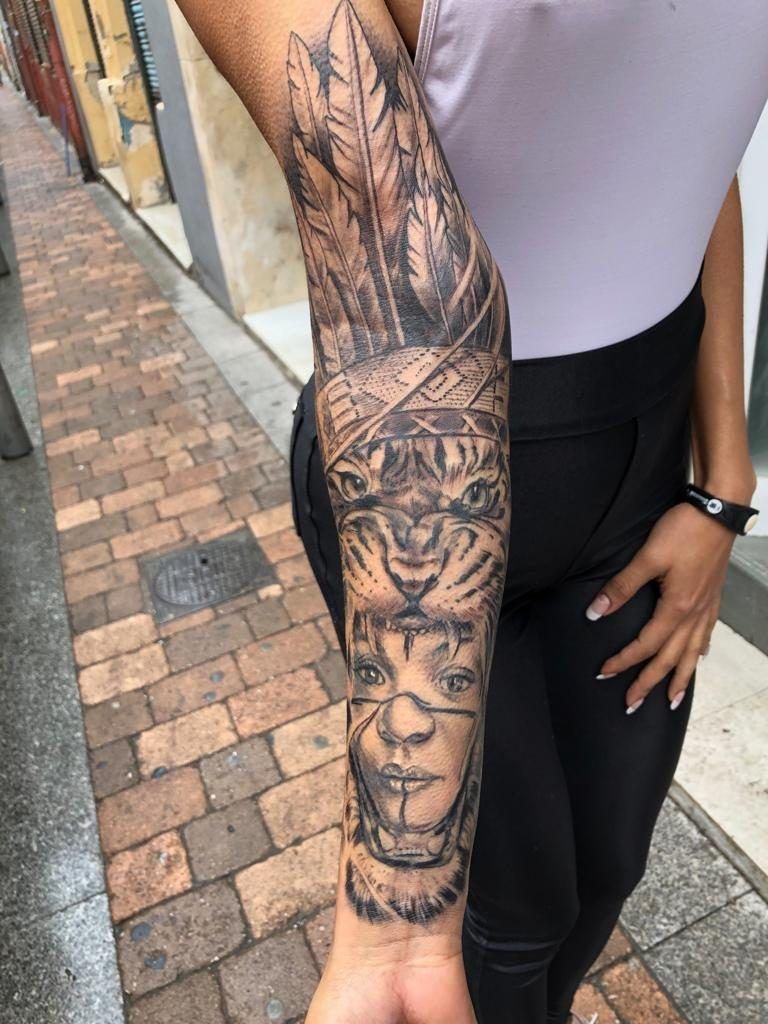 Tatuaje de de un tigre con la boca abierta y en el centro el rostro de una mujer estilo realismo en el antebrazo