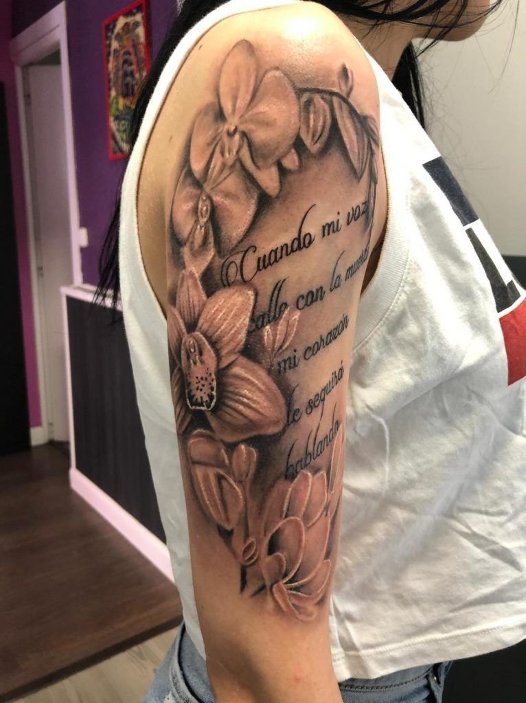 Tatuaje de un poema rodeado de flores en el brazo