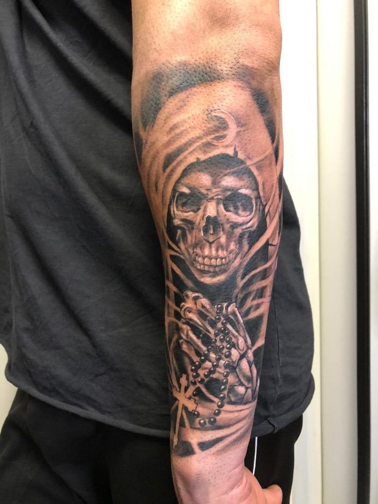Tatuaje de la santa muerte sosteniendo un crucifijo en el antebrazo