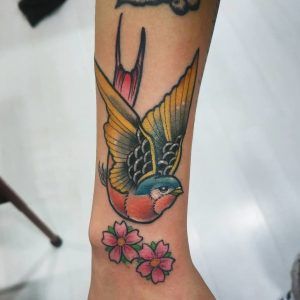 Tatuaje golondrina con dos flores estilo old school en la muñeca