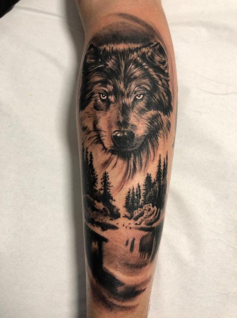 Tatuaje de un de un paisaje con un lobo en el antebrazo