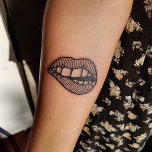 Tatuaje de una boca mordiéndose los labios en el antebrazo