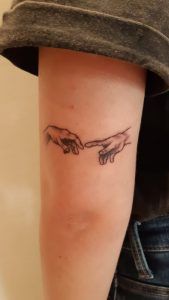 Tatuaje los dedos tocándose de la obra La creación de Adán estilo minimalista en el antebrazo