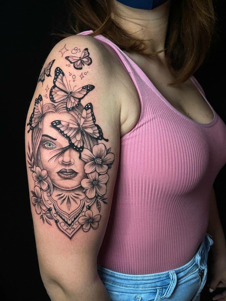 tatuaje de un rostro rodeado de flores y mariposas de estilo realista en el brazo