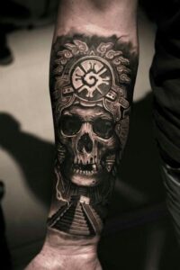 Tatuaje a blanco y negro de una calavera maya con elementos de la cultura maya en el antebrazo