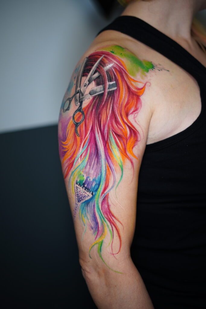 tatuaje watercolor tijera cortando cabello de colores en el hombro