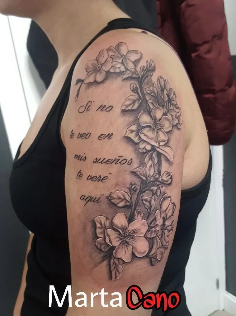 Tatuaje de una frase rodeada de flores estilo realismo en el brazo