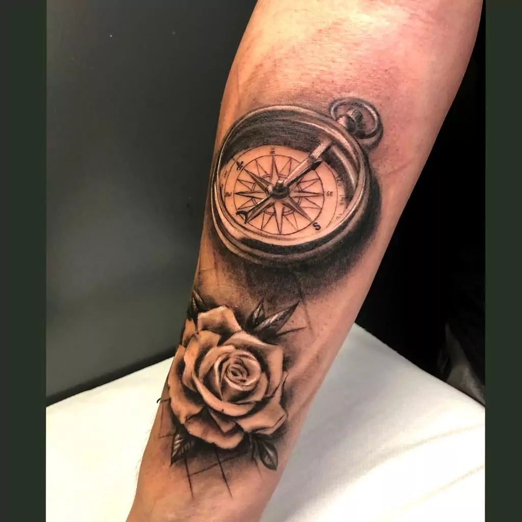 Tatuaje de una brújula con una rosa estilo realismo en el antebrazo
