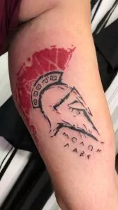 Tatuaje casco gladiador estilo trash polka en el brazo