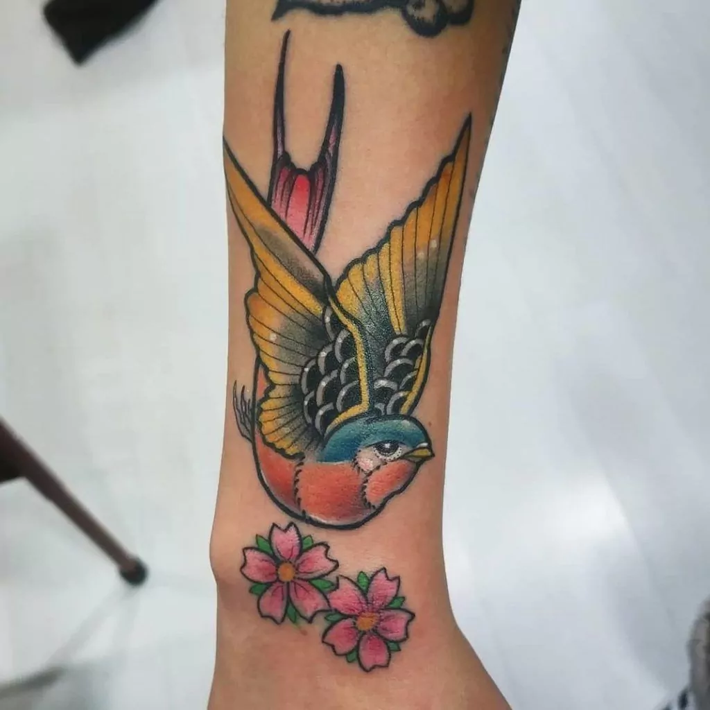 Tatuaje golondrina con dos flores estilo old school en la muñeca