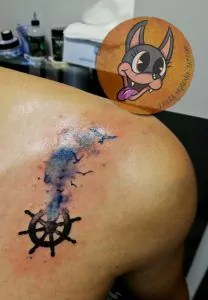 Tatuaje de un timón de un barco con pájaros volando con efecto watercolor en el hombro
