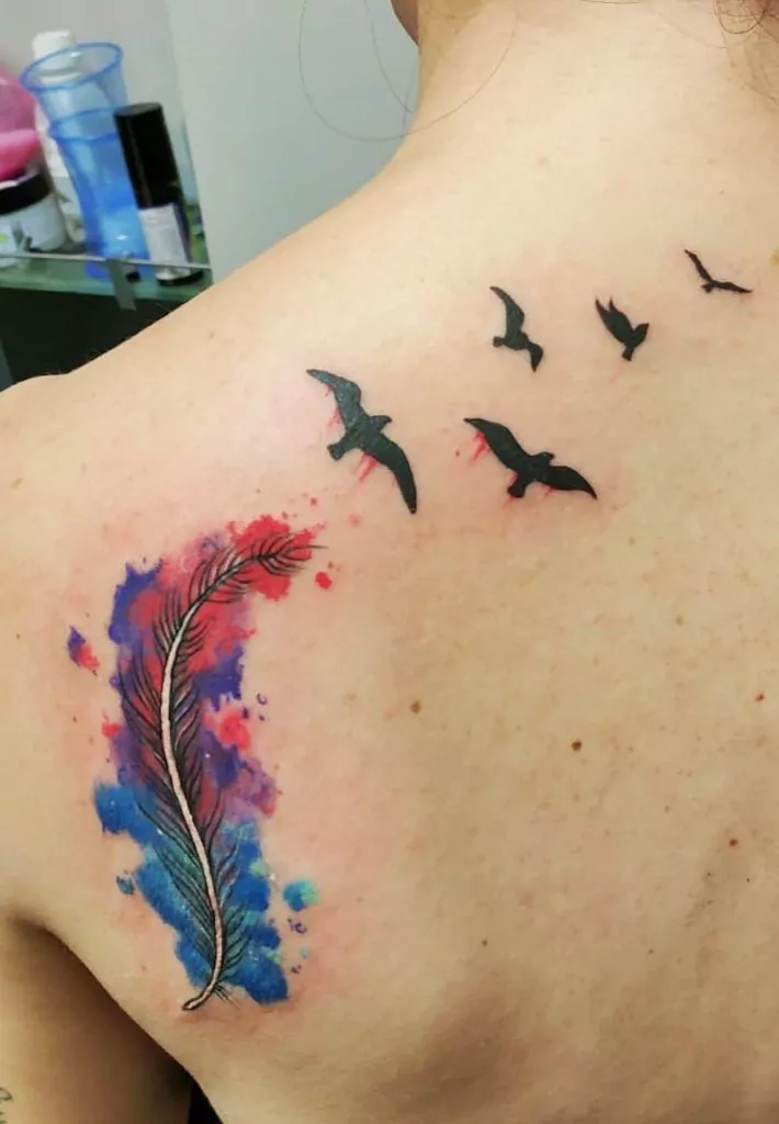 Tatuaje pluma con pájaros volando y efecto watercolor en la espalda