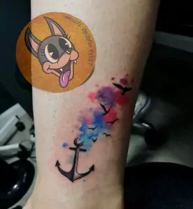 Tatuaje de una ancla con pájaros volando y efecto watercolor en el tobillo