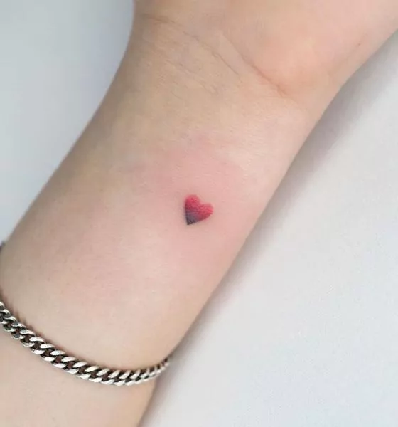 tatuaje minimalista corazón degradado de rojo a negro en la muñeca